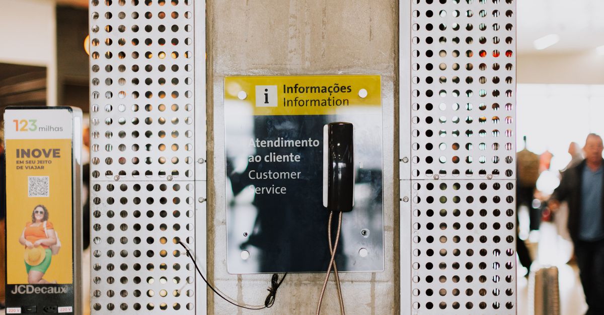 Public phone for customer service at a bustling station entrance with signage.