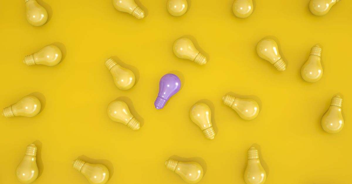 Standout purple light bulb among yellow bulbs on a yellow surface symbolizing individuality.