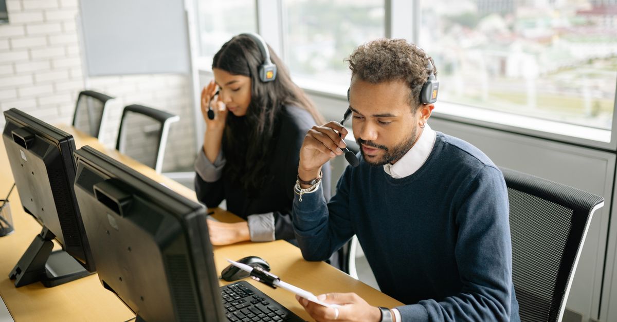 Two call center employees using headsets at their desks in an office environment.