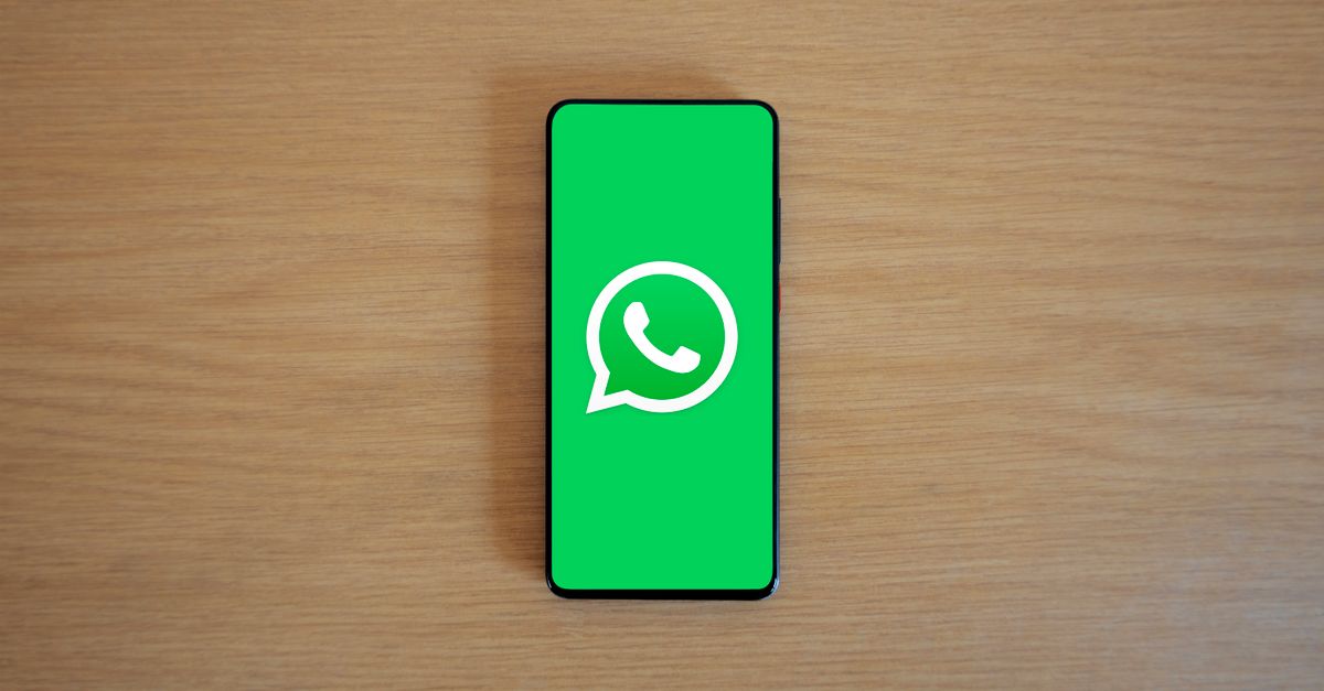 Top view of smartphone displaying WhatsApp logo on a wooden background, representing technology and communication.