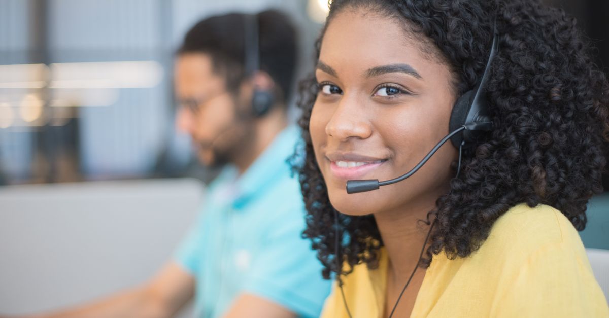 Professional woman with curly hair and headset smiling in a call center environment.