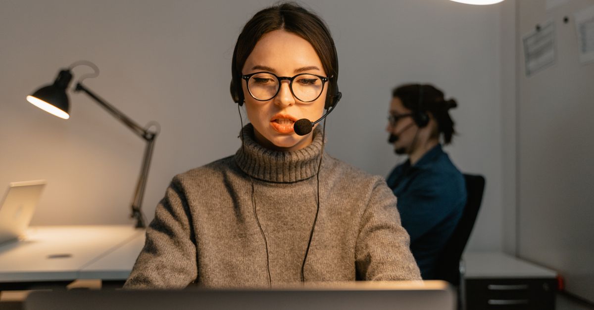 Focused call center agent wearing glasses and headset at work indoors.
