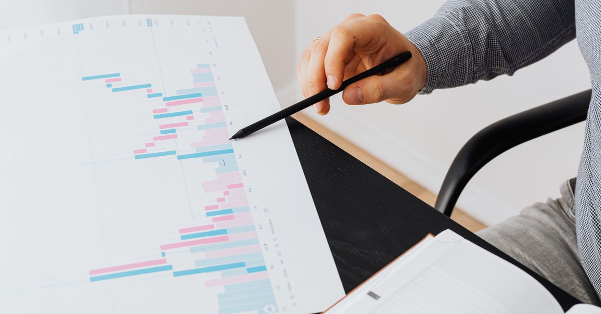 Close-up of a person analyzing a colorful graph chart with a pen in a modern office setting.