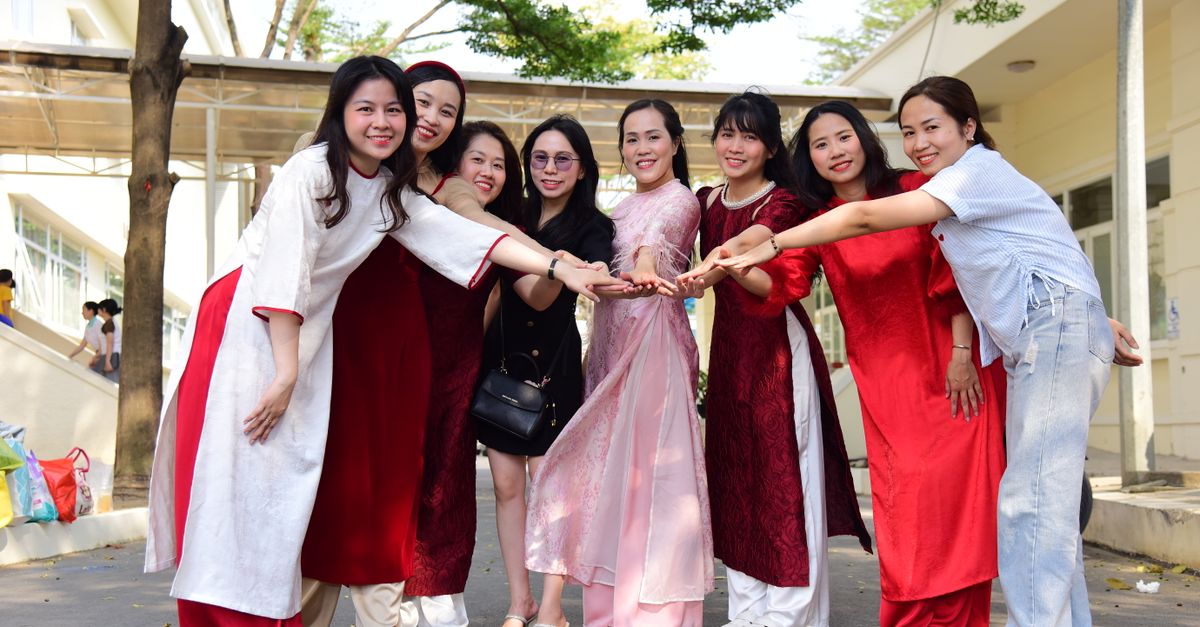 A group of smiling women in traditional Vietnamese dresses gathers outdoors expressing friendship and togetherness.