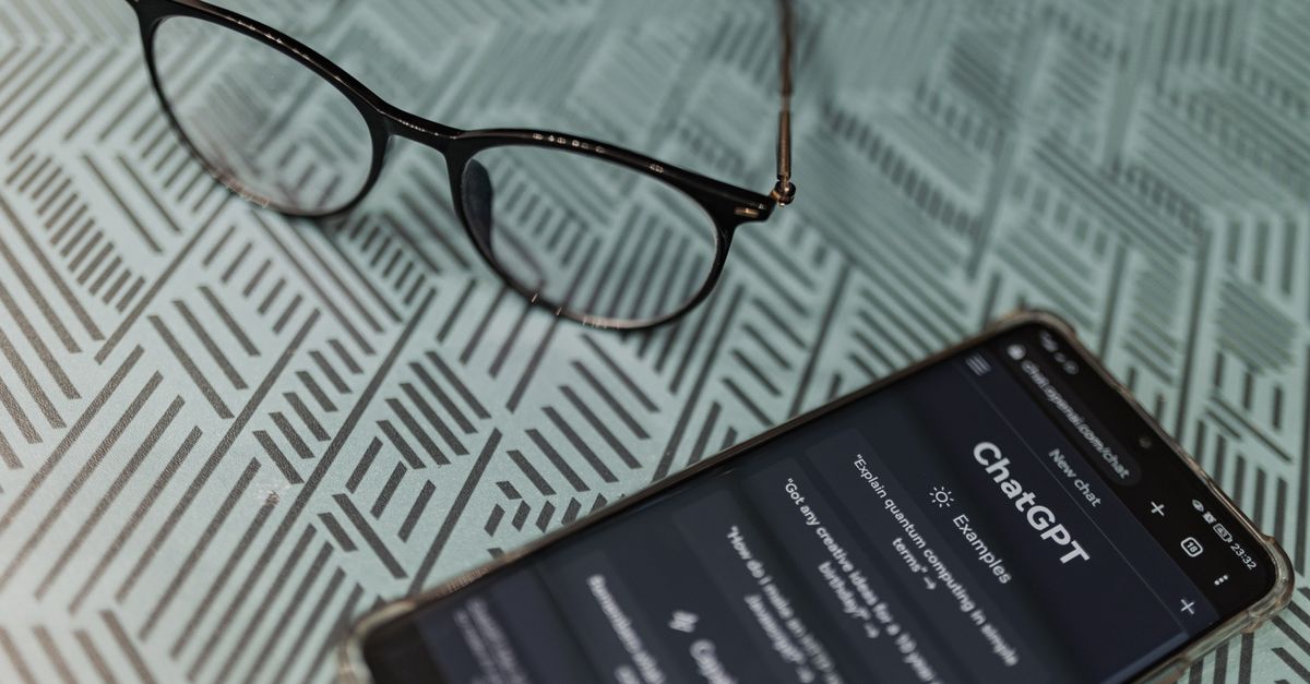 Eyeglasses next to a smartphone displaying the ChatGPT AI app on a patterned surface.